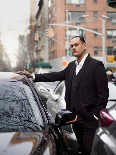 Chofer profesional con traje formal junto a un auto, representando la seguridad para viajes familiares y traslados por razones de salud.