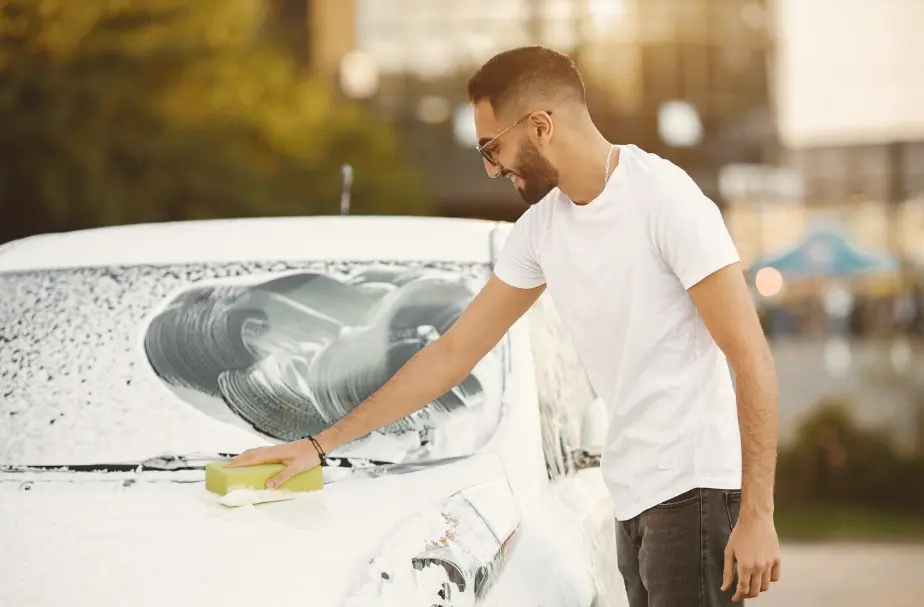 Un joven lavando un auto blanco con espuma, ilustrando el beneficio de limpieza incluido en la custodia de Yo Te Salvo.